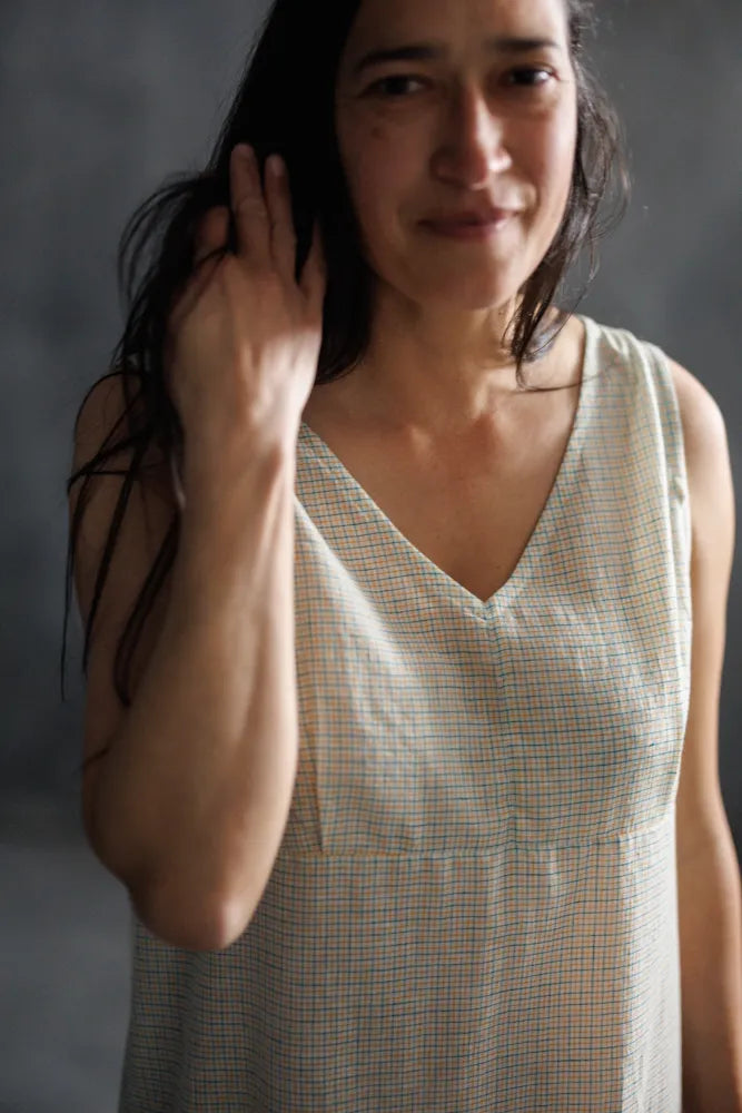 Woman wearing a sleeveless checkered dress made using The Lilian Sewing Pattern by Merchant & Mills against a gray background