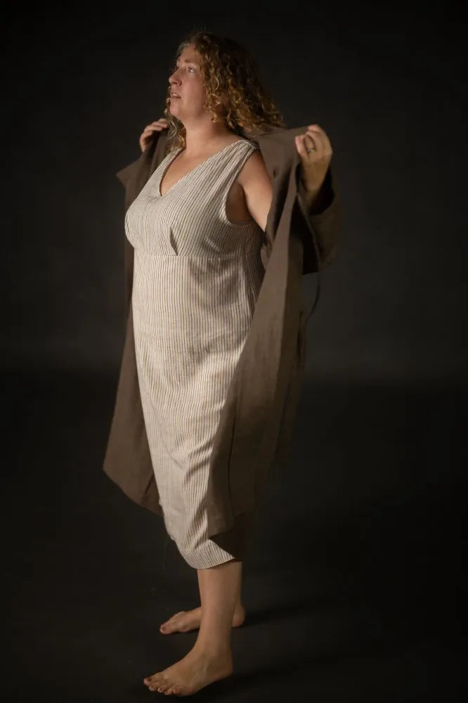 Person wearing a beige dress made using The Lilian Sewing Pattern by Merchant & Mills and coat against a dark background