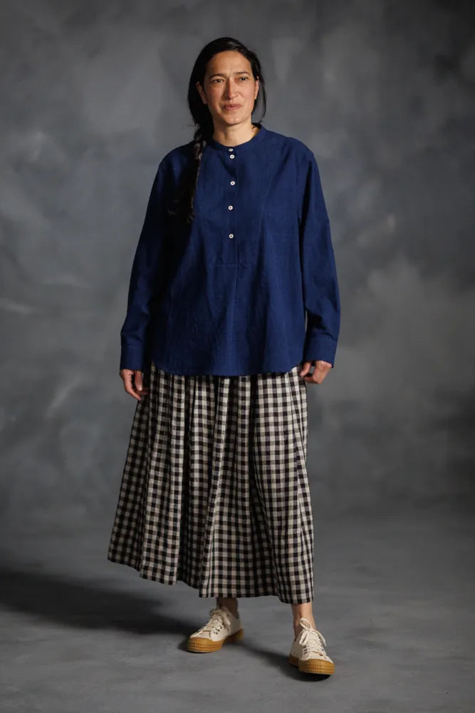 Person wearing a blue top made using The Niven Sewing Pattern by Merchant & Mills  and checkered skirt against a gray background