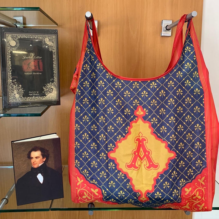 A tote bag with a geometric pattern featuring a prominent gold 'A' on a navy background, reflecting the cover design of Nathaniel Hawthorne's novel The Scarlet Letter.
