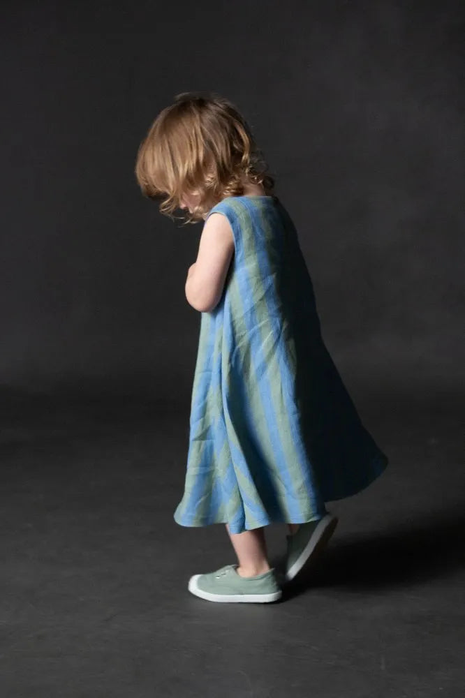 Child wearing a blue striped dress  made using trapezette girls dress sewing patternagainst a dark background