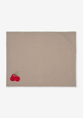 A grey cotton placemat with tomato embroidery at bottom left corner.