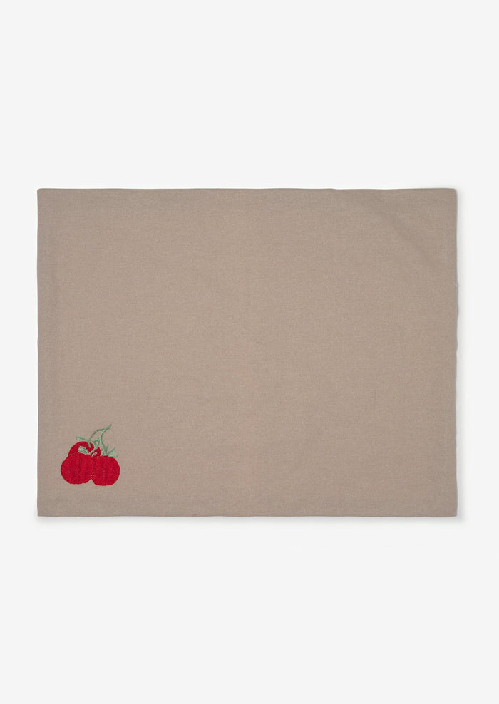 A grey cotton placemat with tomato embroidery at bottom left corner.